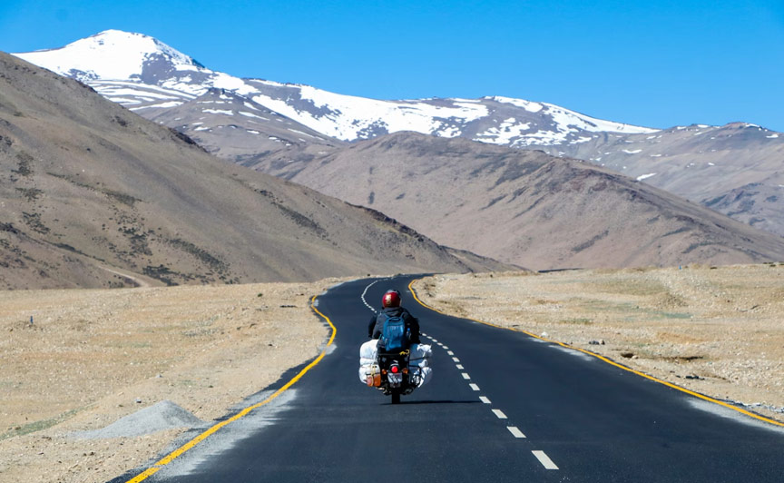 A Caucasian male motorcycle rider expertly maneuvering a winding road, surrounded by stunning snow-capped Himalayan peaks, embodying the spirit of adventure and freedom in a highly realistic style. The image showcases intricate details of the motorcycle, rider, and the mountainous landscape, evoking a sense of exhilaration and liberation from motorcycle touring in India.